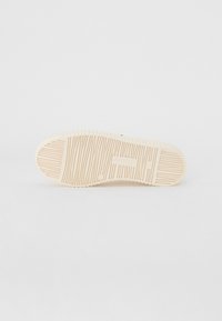 Suela de zapato de goma de color beige claro con surcos y patrones texturizados. Presenta un logo y un emblema de marca redondo cerca del talón.
