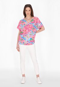 Korte ærmer, V-hals bluse i et særligt blomsterprint med pink, grønne og blå nuancer. Sammen med hvide opsmøgte bukser og hvide sneakers.