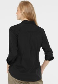 Black button-up shirt with a collar, long sleeves rolled at the cuffs, back pleat detail, and smooth texture.