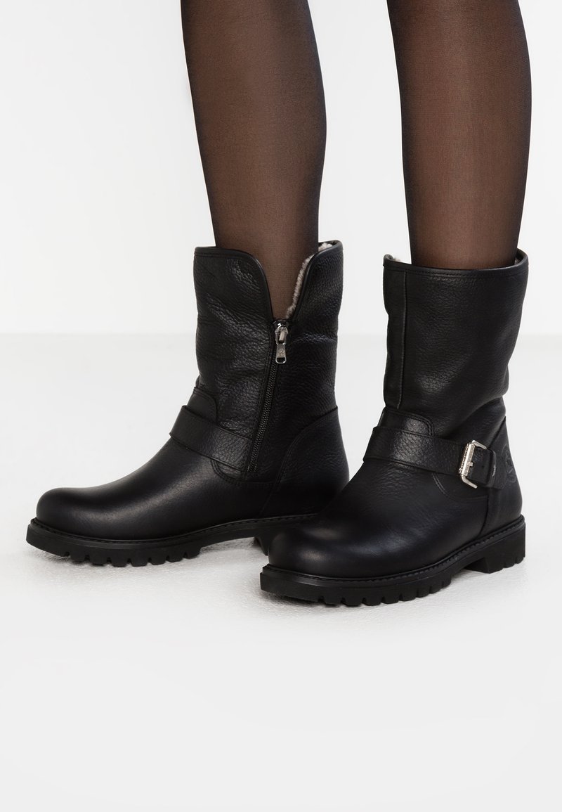 Black leather boots with a textured finish, featuring a side zipper and a strap with a silver buckle. Low, sturdy rubber soles.