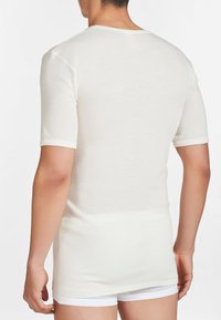 Camicia bianca a maniche corte realizzata in un tessuto morbido e leggero. Design aderente con scollo rotondo e orlo posteriore leggermente più lungo.