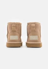 Botines de ante en tono beige con puntera redonda, forro de pelo sintético y suela de goma plana. Presentan una pestaña en la parte trasera y una marca en el talón.