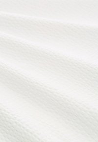Tissu blanc avec un subtil motif texturé en gaufre et de doux plis créant des ombres délicates.