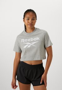 Grå, kortermet t-skjorte med en stor hvit Reebok-logo, kombinert med svarte shorts med elastisk midje. Tøyet ser mykt ut med en uformell passform.