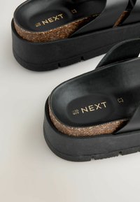 Sandali platform neri con zeppa in sughero, dotati di cinturini larghi e finitura liscia. Logo "NEXT" stampato in oro sulla soletta.