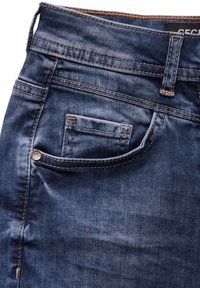 Vaqueros de denim con un lavado azul oscuro, que presentan un bolsillo trasero con un botón plateado y costuras naranjas a lo largo de las costuras y los bordes de los bolsillos.
