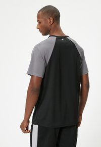Sort og grå atletisk t-shirt med mesh tekstur, korte ærmer, rund hals og logo på ryggen, designet til komfort og bevægelighed.