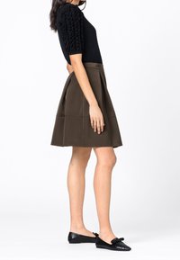 Černý krátký rukáv triko s texturovanými nadýchanými rukávy, spárované s olivově zelenou sukní a černými plochými botami s mašlí.