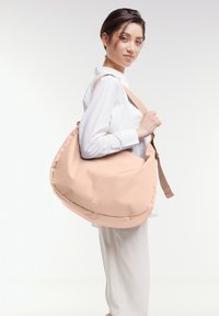 Borsa a spalla in tessuto rosa chiaro con forma arrotondata, tracolla regolabile e un piccolo dettaglio del logo. Texture liscia e design minimalista.