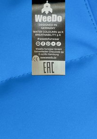 Niebieska tkanina o gładkiej fakturze, z etykietą z czarnym tekstem wskazującym markę, miejsce pochodzenia wzoru oraz specyfikacje produktu dotyczące wodoodporności.