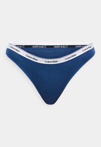 Blå bomullstanga med en midjebånd som har et hvitt bånd merket "Calvin Klein." Stoffet har en glatt tekstur.