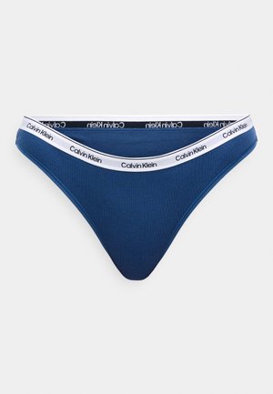 Niebieskie bawełniane stringi z paskiem obejmującym białą taśmę z napisem "Calvin Klein". Materiał ma gładką teksturę.