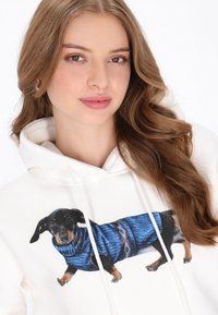 Sudadera con capucha blanca con un gran estampado de un dachshund con un suéter azul de punto con patrones geométricos. Tela suave con cordones ajustables.