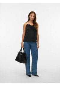 Svart sateng-camisole med blonderkant, kombinert med vide blå denimjeans. Modellen holder en svart skinnveske og har på spisse sko.