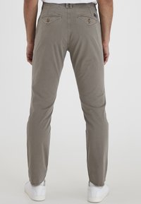 Grå chinos laget av bomull, med rett ben-design, to baklommer med knappelukking, og brukt med hvite sneakers.