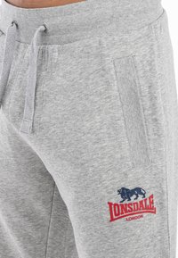 Grå bomulds sweatpants med strammemiddel og sidelommer, der har et rødt broderet "Lonsdale London" logo med en løve grafik.