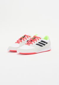 Zapatillas deportivas blancas con rayas negras, cordones rosas y detalles en verde brillante. Fabricadas con una combinación de materiales sintéticos y tela.