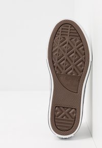 Braune Gummisohle mit gemustertem Profil, weißen Seitenwänden und geprägtem Branding, das ein klassisches Converse All Star Design aufweist.