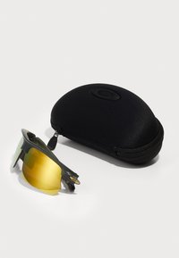 Sportsonnenbrille mit grünem Rahmen und gelb getöntem Glas, begleitet von einem schwarzen Hartschalenetui mit einem Reißverschluss und Logo.