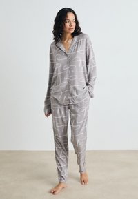 Ensemble de pyjama gris comprenant une chemise à boutons et un pantalon assorti, avec un motif abstrait blanc, une texture douce et des manches longues.