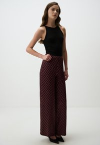 Zwarte mouwloze top gecombineerd met high-waisted, wijde broek met een geometrisch patroon in rood en marineblauw. Zwarte puntige hakken inbegrepen.