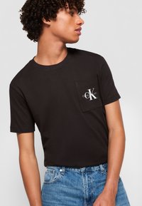 Zwarte katoenen T-shirt met korte mouwen en een ronde hals, voorzien van een borstzak met een wit "Calvin Klein Jeans" logo.