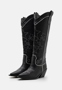 Black leather cowboy boots with pointed toes, featuring white stitching and star patterns along the shaft. Wedge heel design.