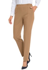 Tan stretchbroek met een comfortabele elastische tailleband, een getailleerde pasvorm en verticale naaddetails, gecombineerd met zwarte hoge hakken.