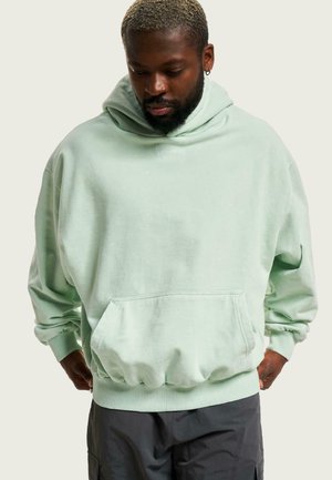 Mintgrøn oversized hættebluse i blødt materiale, med en kengurulomme, ribbede manchetter og hætte med snoretræk. Enkel broderet detalje.