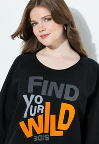 Felpa nera con una grande stampa grafica che recita "FIND Your WILD SIDE" in grigio e arancione. Tessuto morbido e casual con vestibilità rilassata.