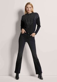 Zwarte lange mouwen top met pailletten verticale patronen, gecombineerd met zwarte flared jeans met sprankelende accenten aan de randen en enkel.