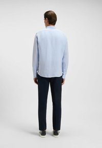 Jasnoniebieska koszula z długim rękawem, o okrągłym dolnym wykończeniu, z zapięciem na guziki przy mankietach i miękką teksturą, zestawiona z ciemnymi spodniami i casualowymi butami.