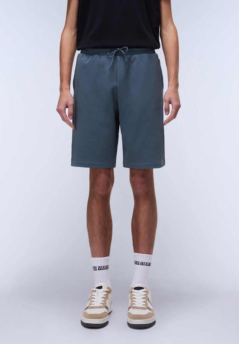 Shorts grigi in cotone con un elastico in vita e cordino, caratterizzati da una vestibilità comoda. Abbinati a calzini bianchi e sneakers beige.