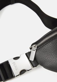 Borsa in vita nera in pelle con superficie texturizzata, zip argentata e un gancio metallico con il nome del marchio BOSS. Inclusa una tracolla regolabile.
