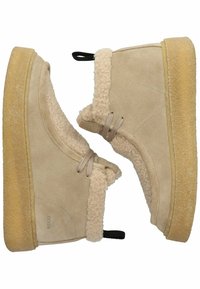 Bottines en suede beige avec doublure en shearling douce, lacets élastiques et semelle en caoutchouc. Équipées d'une languette noire pour un enfilage facile.