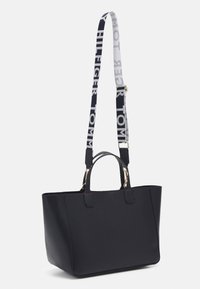 Sac à main rectangulaire noir avec deux poignées courtes et une bandoulière longue noir et blanche portant le texte "Tommy Hilfiger".