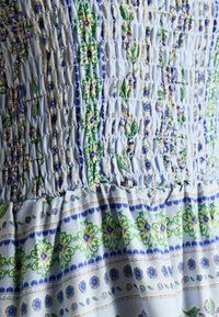 Svetlomodrá tkanina s nariasenou textúrou, zdobená kvetinovými vzormi v zelenej, žltej a modrej farbe, doplnená horizontálnymi pruhmi a jemnými detailmi.