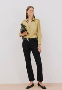 Camicetta in satin verde oliva, jeans neri a vita alta, ballerine nere con borchie e una pochette nera. Design semplice con dettagli in bottoni.
