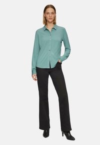 Lichtblauwe button-up shirt met een kraag, lange mouwen en slim fit, gecombineerd met zwarte flare-broeken en zwarte hakken.