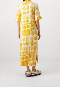 Robe à manches longues et courtes présentant un motif jaune et blanc avec différentes formes et designs. Fentes latérales pour faciliter le mouvement. Coupe décontractée.