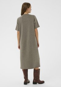 Olīvu zaļš, līdz ceļiem garš kleita ar īsām piedurknēm, izgatavota no mīksta auduma, ar taisnu griezumu un sānu šķēršļiem, apvienota ar brūnām ādas zābakiem.