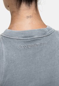 Grijze katoenen sweatshirt met gebreide ronde hals, met de geborduurde tekst "GOODFORnothing" op de achterkant nabij de nek en een zichtbare tatoeage.
