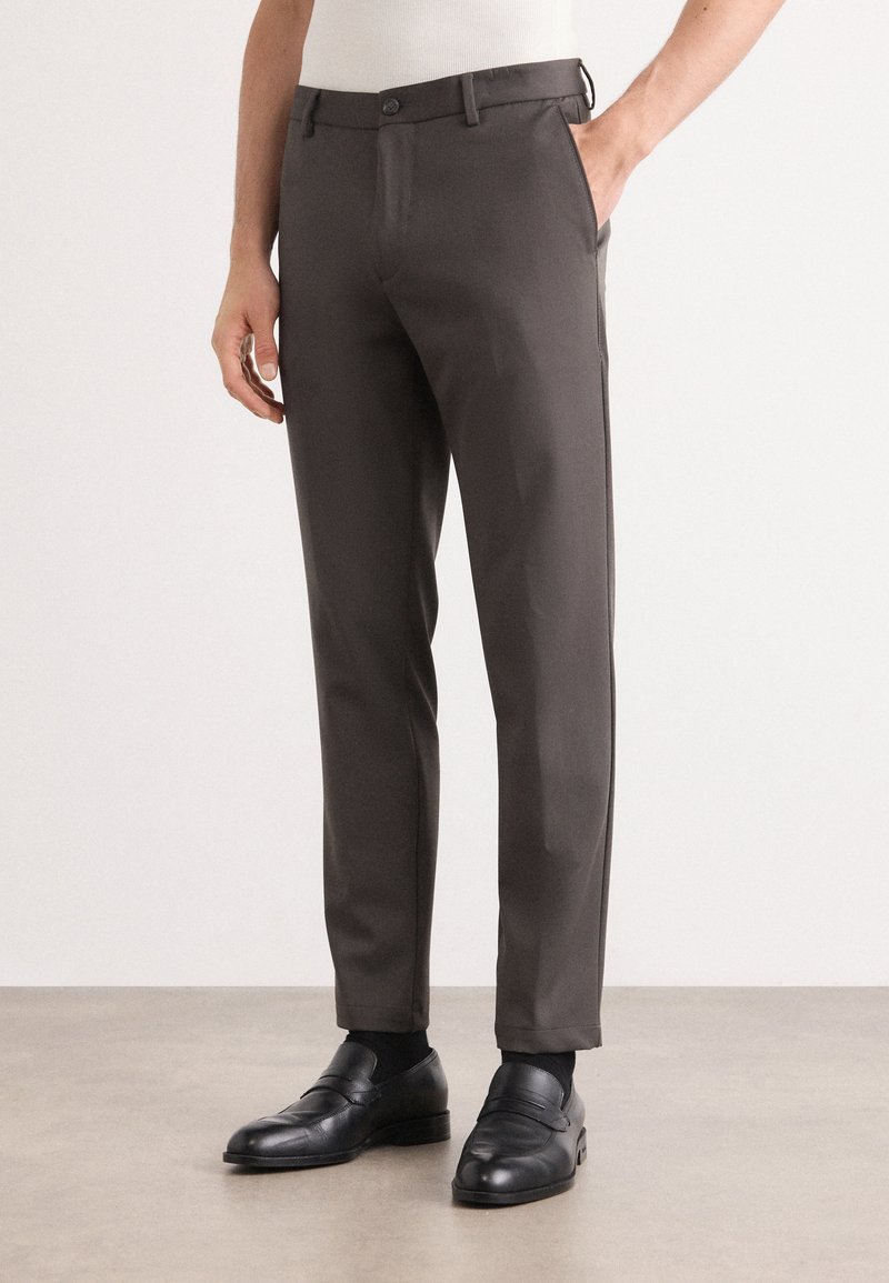 Gray tailored trousers with a slim fit, made of smooth fabric. Features a button closure and side pockets. Paired with black loafers.