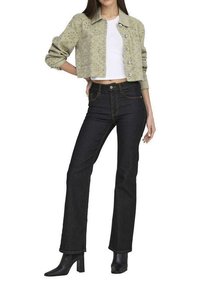 Veste cropped vert clair avec des détails en fleurs découpés, associée à un jean flare en denim foncé et des bottines noires.