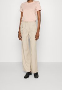 Beige wide-leg trousers with side pockets, paired with a pale pink fitted t-shirt, worn with black heeled shoes. Smooth fabric texture.