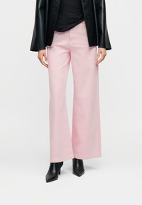 Ροζ παντελόνια ευρέος ποδιού από βαμβάκι, με μέση μεσαίου ύψους και λεία υφή, σε συνδυασμό με μαύρες μπότες με μυτερές μύτες και ψηλό τακούνι.