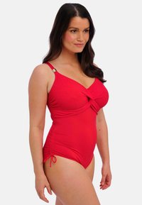 Maillot de bain une pièce rouge avec un design croisé à l'avant, un tissu texturé, des bretelles réglables et des détails froncés sur les côtés. Accents en or.
