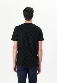 T-shirt noir à manches courtes avec un motif texturé de petites formes florales. Tissu doux et coupe décontractée. Porté avec un jean bleu.
