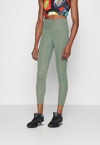 Leggings verdi realizzati in tessuto elasticizzato con una vita alta, abbinati a un crop top colorato e scarpe da ginnastica nere.