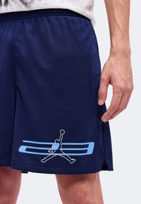 Gros plan d'une personne portant un short de basket bleu marine avec un logo Jumpman bleu clair et blanc près de l'ourlet et un t-shirt blanc et noir.
